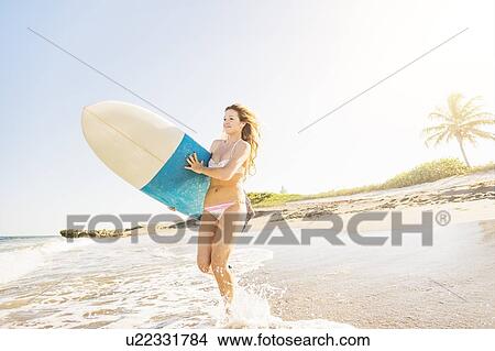 Young woman running in surf into sea carrying surfboard View Large Photo Image Picture - Young woman running in surf into sea carrying surfboard. Fotosearch