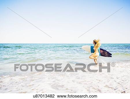 Young woman running in surf into sea carrying surfboard View Large Photo Image Stock Image - Young woman running in surf into sea carrying surfboard. Fotosearch