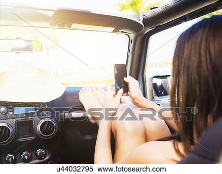 Young woman sitting in car with legs on dashboard using smart phone View Large Photo Image Stock Photography - Young woman sitting in car with legs on dashboard using smart phone. Fotosearch
