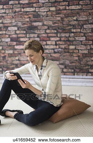 Stock Image - Young woman sitting on floor and using digital tablet. Fotosearch