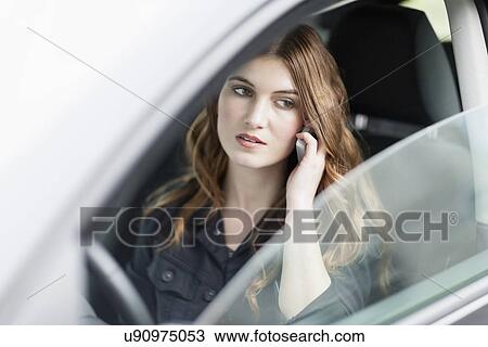 Stock Image - Young woman speaking on phone in car. Fotosearch