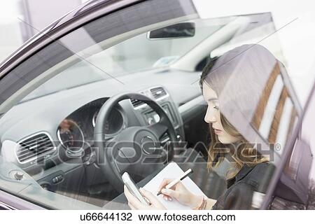 Stock Image - Young woman writing in notebook in car. Fotosearch