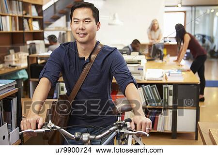 Picture - Architect Arrives At Work On Bike Pushing It Through Office. Fotosearch