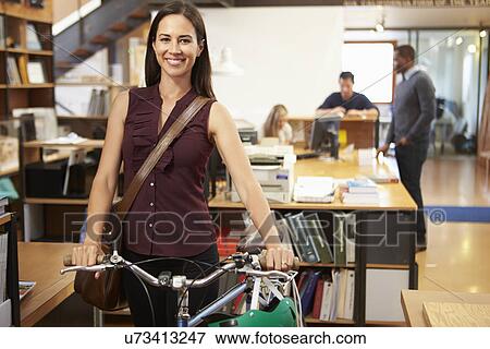 Stock Photo - Architect Arrives At Work On Bike Pushing It Through Office. Fotosearch
