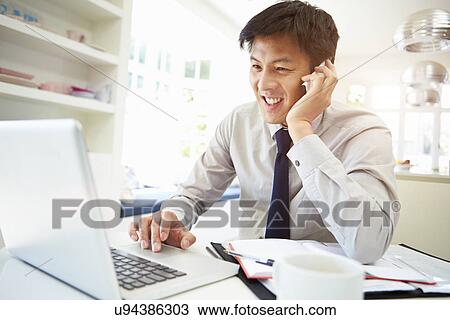 Stock Image - Asian Businessman Working From Home Using Mobile Phone. Fotosearch