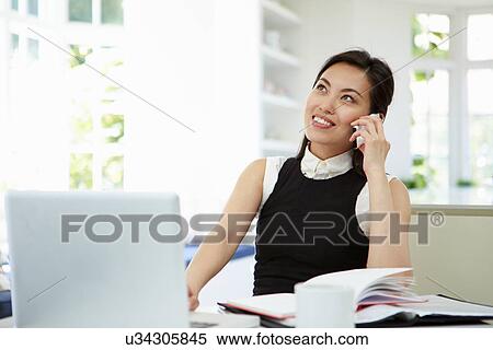 Stock Photography - Asian Businesswoman Working From Home Using Mobile Phone. Fotosearch