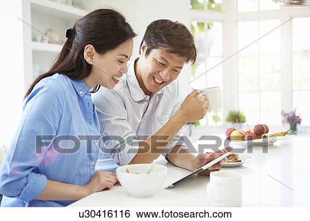 Asian Couple Looking At Digital Tablet Over Breakfast View Large Photo Image Stock Photograph - Asian Couple Looking At Digital Tablet Over Breakfast. Fotosearch