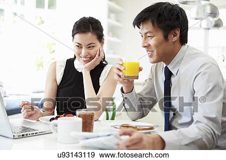 Stock Photo - Asian Couple Looking at Laptop Over Breakfast. Fotosearch