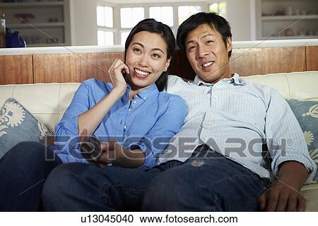 Asian Couple Sitting On Sofa Watching TV Together View Large Photo Image Stock Image - Asian Couple Sitting On Sofa Watching TV Together. Fotosearch