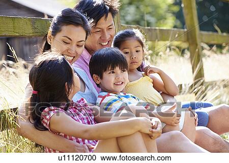 Stock Image - Asian Family Relaxing By Gate On Walk In Countryside. Fotosearch