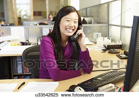 Stock Photography - Asian Woman On Phone In Busy Modern Office. Fotosearch