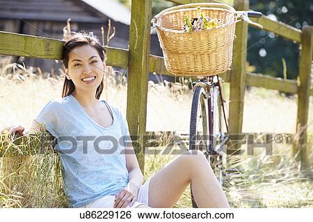 Stock Photograph - Asian Woman Resting By Fence With Old Fashioned Cycle. Fotosearch