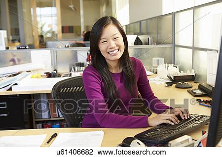 Stock Image - Asian Woman Working At Computer In Modern Office. Fotosearch