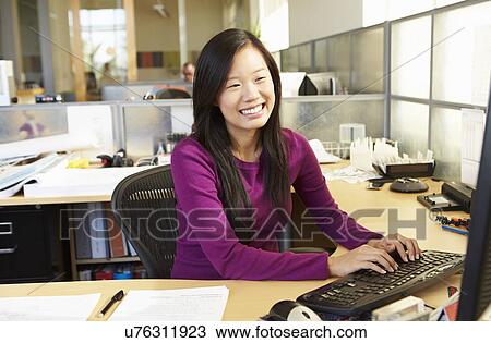 Stock Image - Asian Woman Working At Computer In Modern Office. Fotosearch
