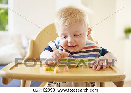 Stock Image - Baby Boy Eating Fruit In High Chair. Fotosearch
