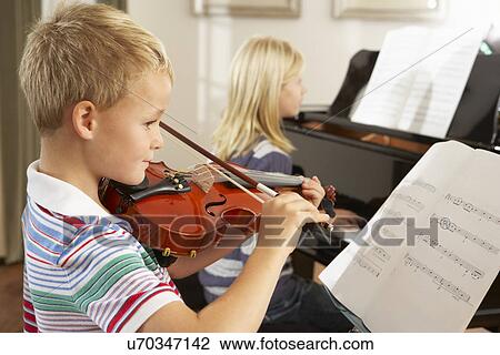 Stock Image - Boy and girl playing violin and piano at home. Fotosearch