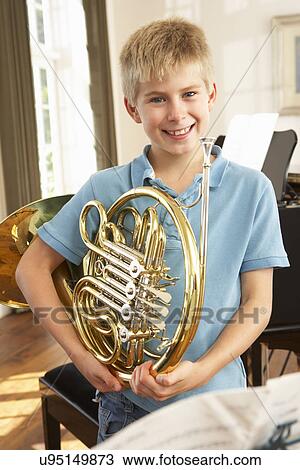 Stock Image - Boy holding French horn at home. Fotosearch