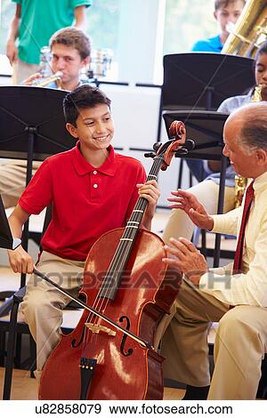 Stock Photo - Boy Learning To Play Cello In High School Orchestra. Fotosearch