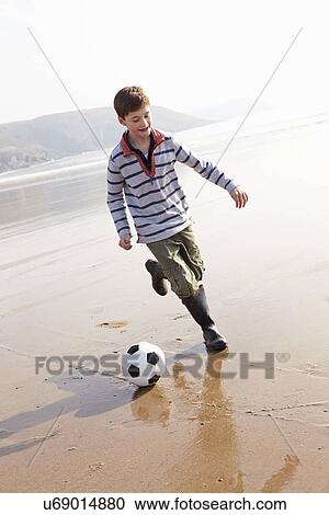 Stock Image - Boy Playing Football On Winter Beach. Fotosearch