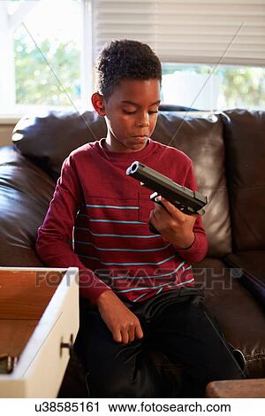 Stock Image - Boy Playing With Parent's Gun He Has Found At Home. Fotosearch