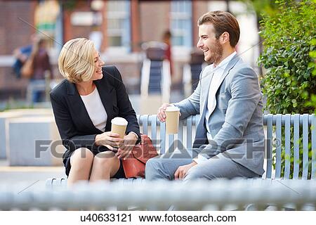 Stock Image - Business Couple On Park Bench With Coffee. Fotosearch