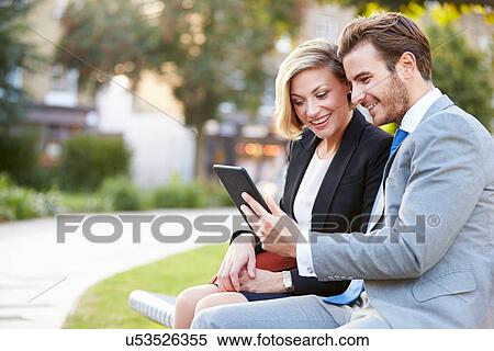 Stock Photography - Business Couple Using Digital Tablet On Park Bench. Fotosearch