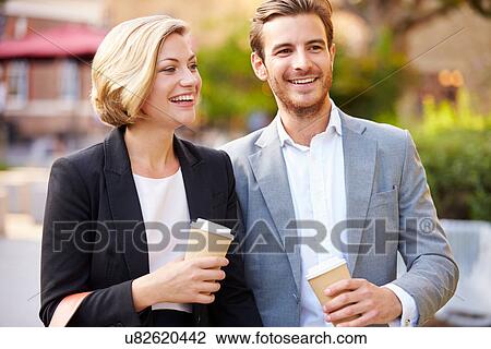Stock Image - Business Couple Walking Through Park With Takeaway Coffee. Fotosearch