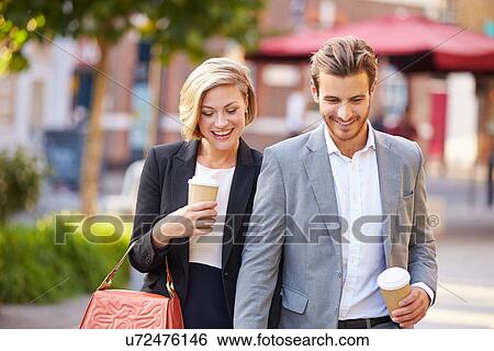 Stock Photograph - Business Couple Walking Through Park With Takeaway Coffee. Fotosearch