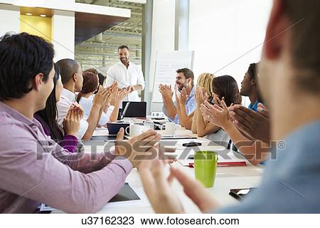 Stock Image - Businessman Addressing Meeting Around Boardroom Table. Fotosearch