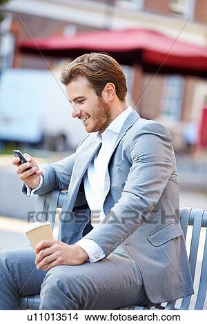 Picture - Businessman On Park Bench With Coffee Using Mobile Phone. Fotosearch