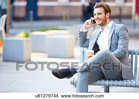 Picture - Businessman On Park Bench With Coffee Using Mobile Phone. Fotosearch