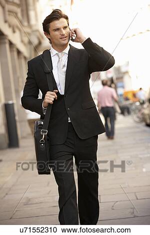 Businessman on phone walking down street View Large Photo Image Stock Image - Businessman on phone walking down street. Fotosearch