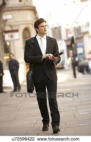 Stock Image - Businessman with tablet walking down street. Fotosearch