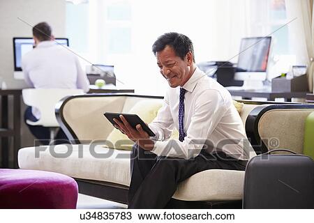 Businessman Working On Digital Tablet In Hotel Lobby View Large Photo Image Stock Image - Businessman Working On Digital Tablet In Hotel Lobby. Fotosearch