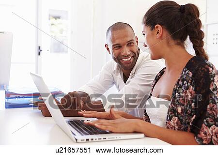 Stock Image - Businesspeople Using Laptop In Office Of Start Up Business. Fotosearch