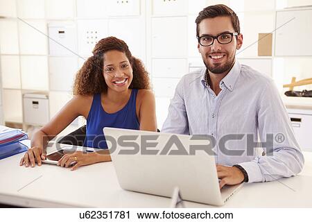 Stock Image - Businesspeople Using Laptop In Office Of Start Up Business. Fotosearch