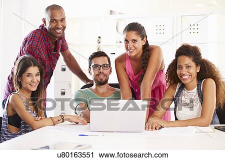 Stock Image - Businesspeople Using Laptop In Office Of Start Up Business. Fotosearch