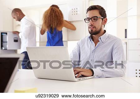 Businesspeople Using Laptop In Office Of Start Up Business View Large Photo Image Stock Photo - Businesspeople Using Laptop In Office Of Start Up Business. Fotosearch