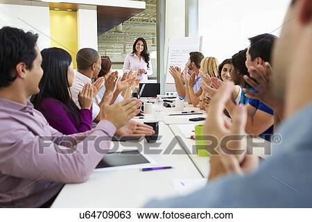 Stock Image - Businesswoman Addressing Meeting Around Boardroom Table. Fotosearch