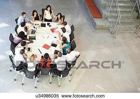 Stock Photography - Businesswoman Addressing Meeting Around Boardroom Table. Fotosearch