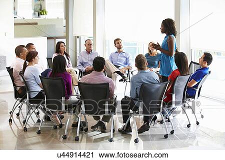 Stock Image - Businesswoman Addressing Multi-Cultural Office Staff Meeting. Fotosearch