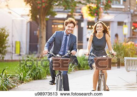 Stock Image - Businesswoman And Businessman Riding Bike Through City Park. Fotosearch