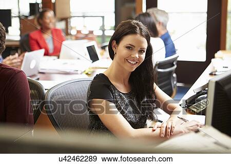 Stock Photo - Businesswoman Working At Desk With Meeting In Background. Fotosearch
