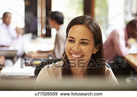 Stock Photo - Businesswoman Working At Desk With Meeting In Background. Fotosearch