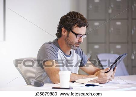 Stock Image - Casually Dressed Man Using Digital Tablet In Design Studio. Fotosearch