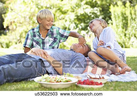 Stock Image - children tormenting father on picnic. Fotosearch