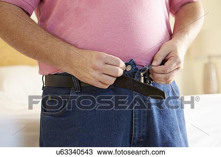Stock Image - Close Up Of Overweight Man Trying To Fasten Trousers. Fotosearch