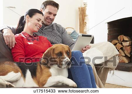 Stock Image - Couple At Home With Pet Dog Looking At Digital Tablet. Fotosearch