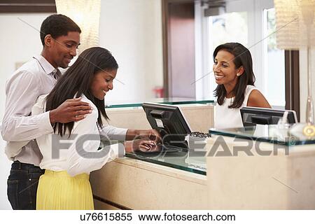 Stock Photography - Couple Checking In At Hotel Reception Using Digital Tablet. Fotosearch