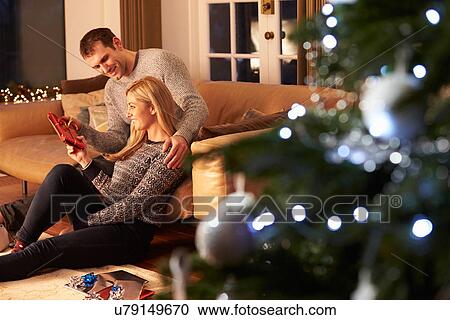 Stock Image - Couple Exchanging Gifts By Christmas Tree. Fotosearch